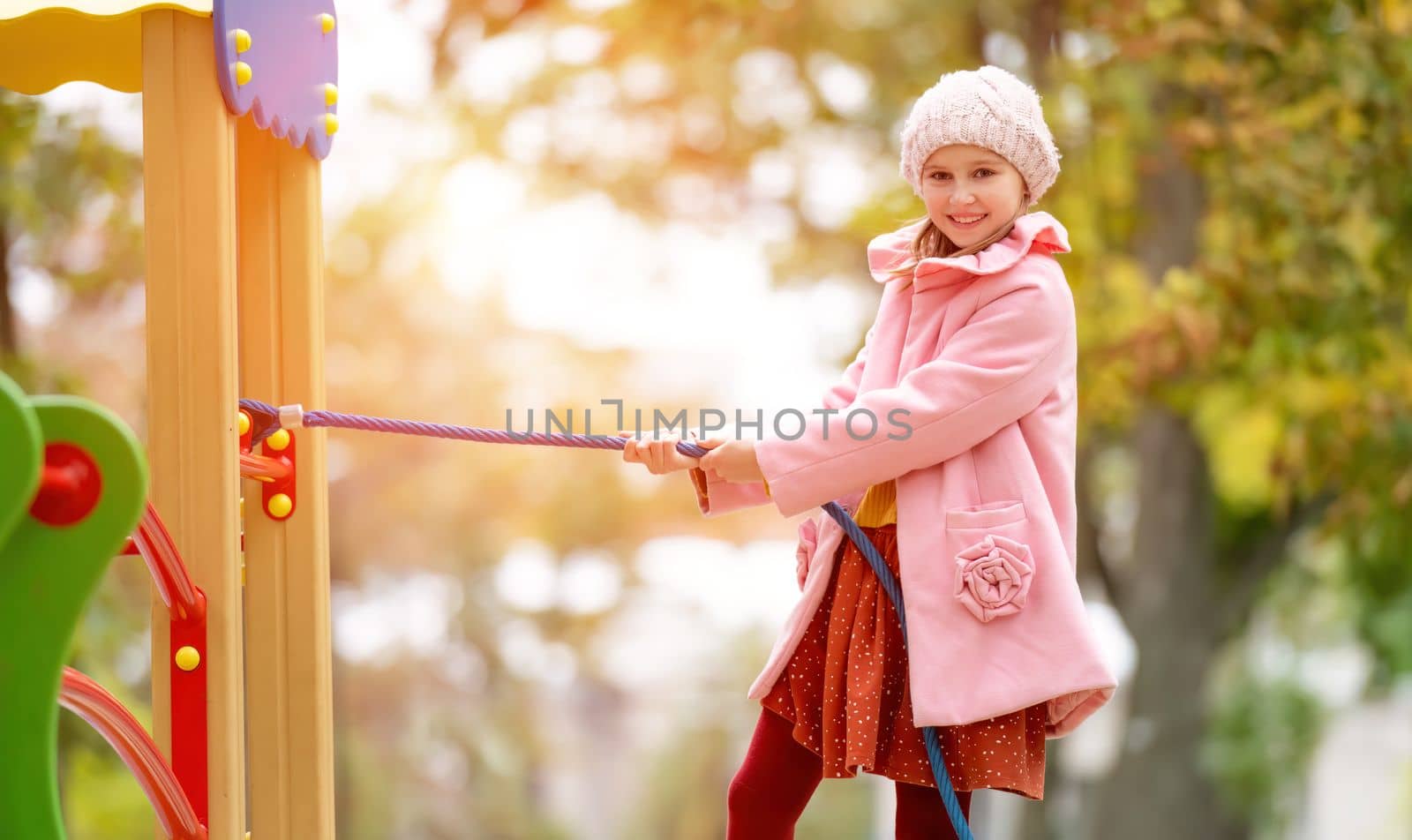 Preteen girl kid climbing on playground at autumn park and smiling. Happy female child portrait outdoors