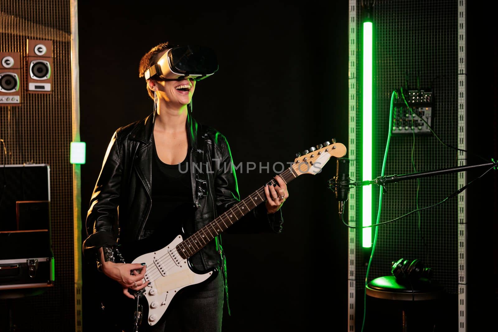 Guitarist with virtual reality headset enjoying rock concert simulation while playing heavy metal song at electric guitar in music studio. Woman musician performing grunge album using electricinstrument