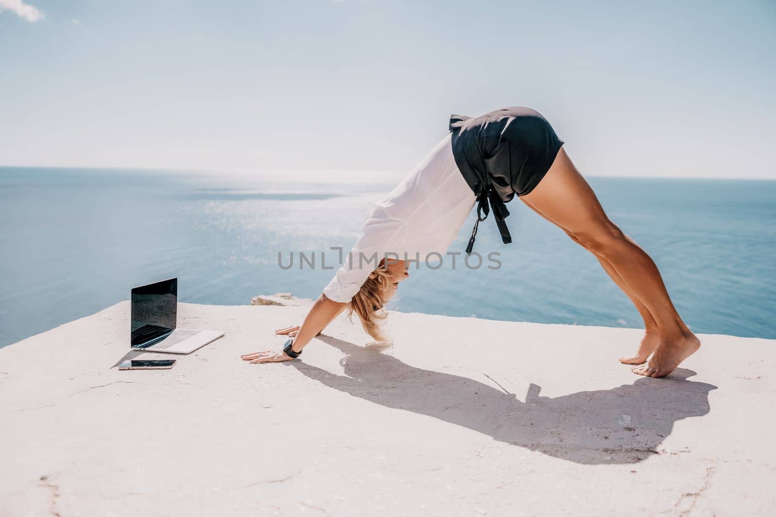 Happy girl doing yoga with laptop working at the beach. beautiful and calm business woman sitting with a laptop in a summer cafe in the lotus position meditating and relaxing. freelance girl remote work beach paradise