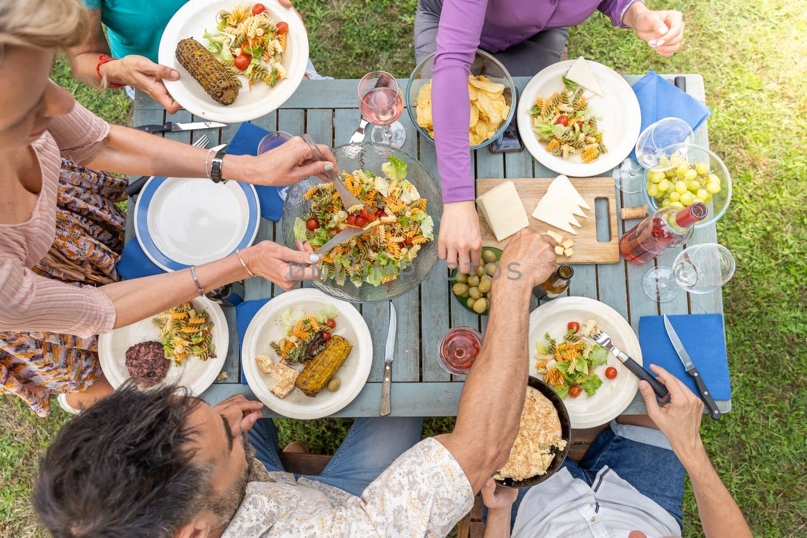 Top view of wooden table with food. Friends having dinner during a sunny day. by PaulCarr