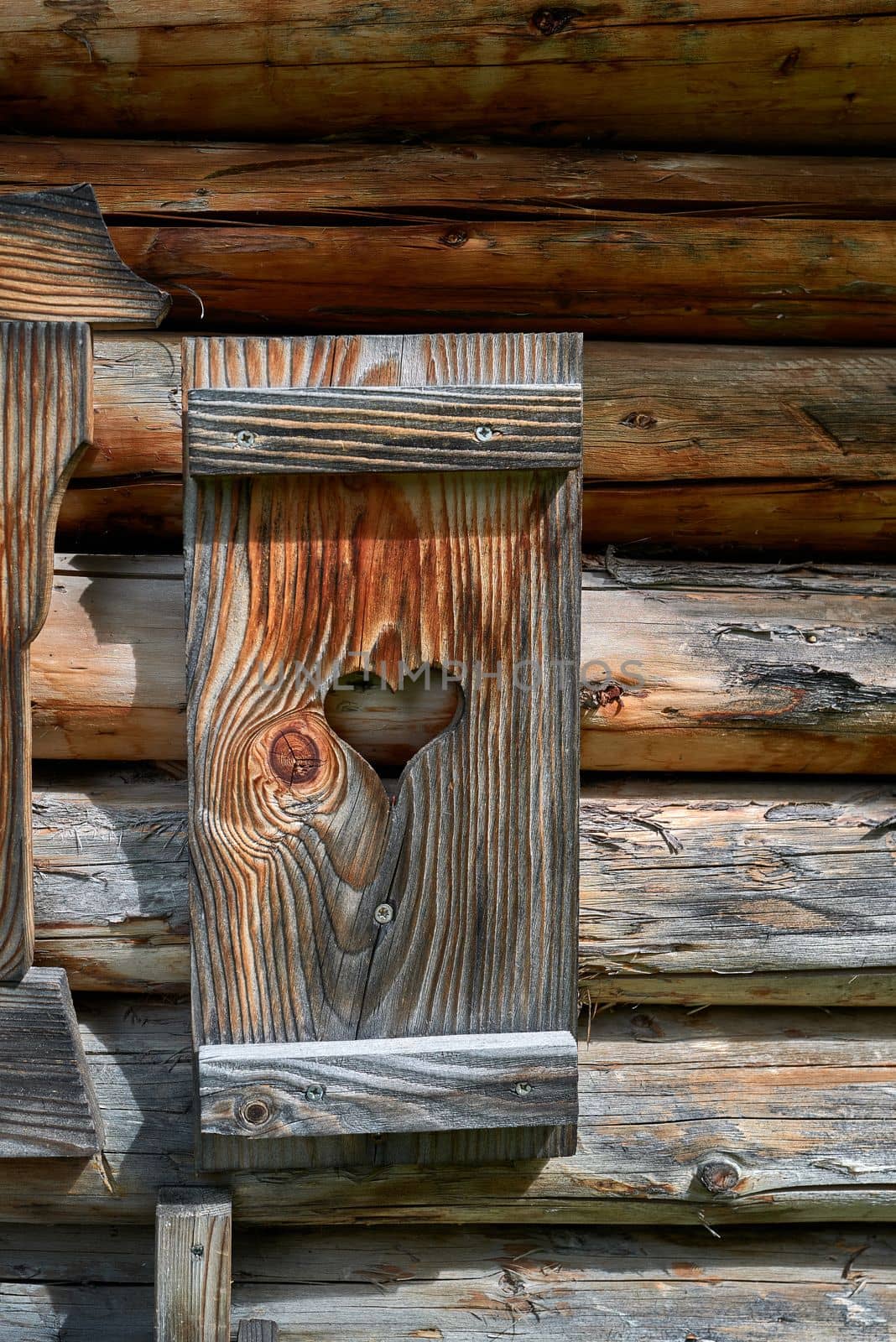 A window shutter decorated with a heart at a small wooden alpine hut.