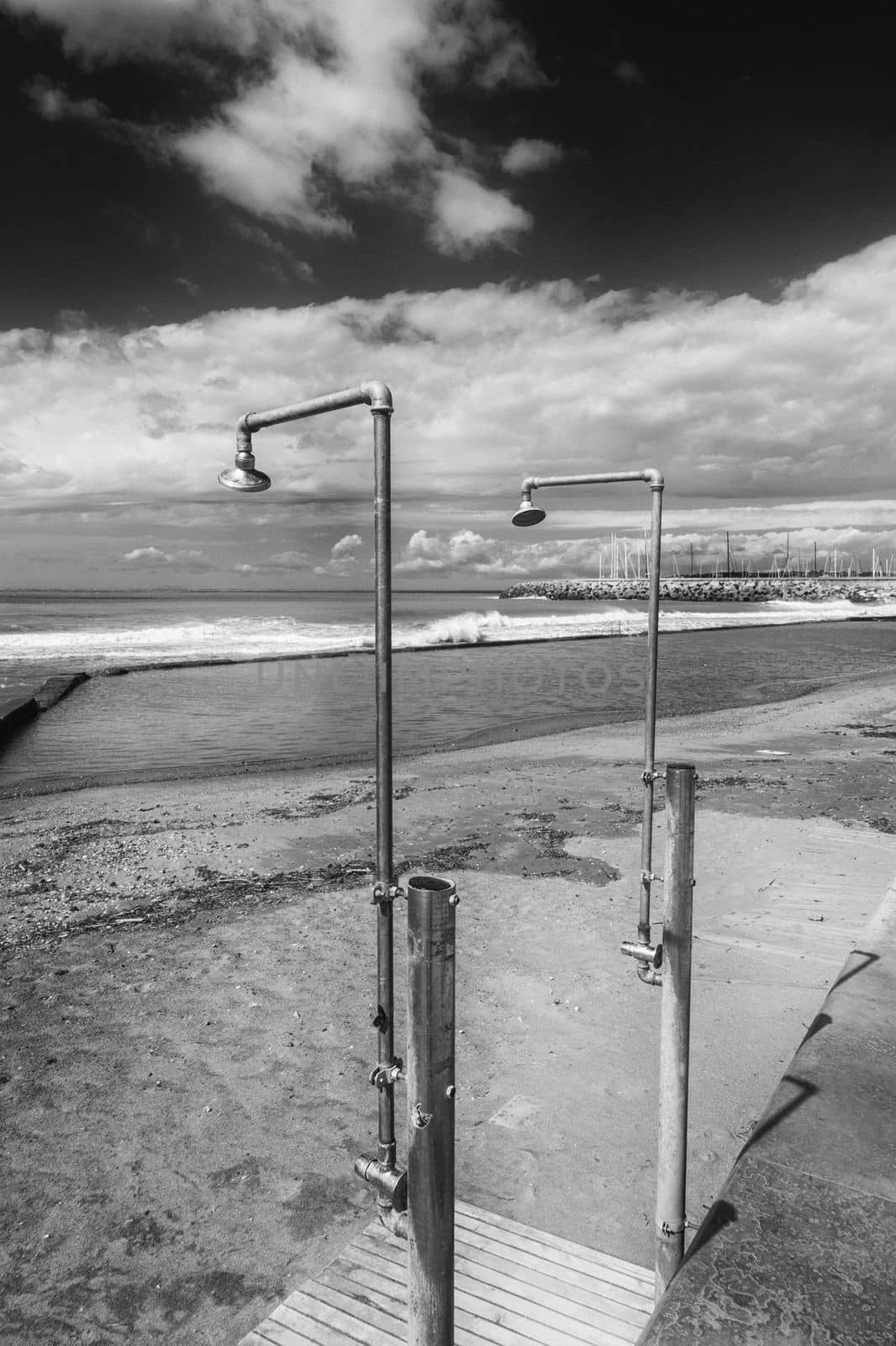 On a deserted sandy beach there are two ageing showers waiting for bathers.