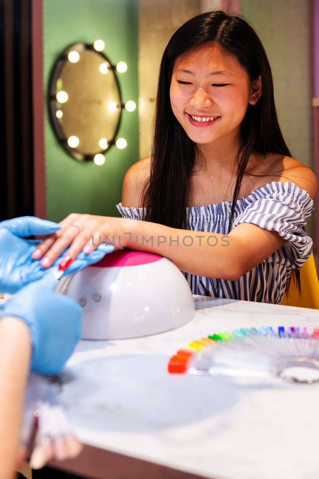 beautiful asian woman trying on nail polish colors during a manicure treatment at the beauty salon, wellness and body care concept