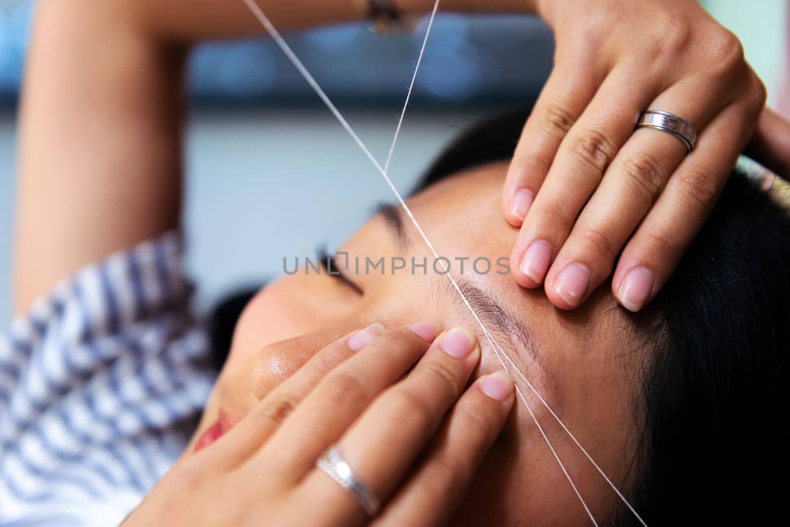 detail of an eyebrow waxing with threading on a young woman in a beauty salon, concept of wellness and body care