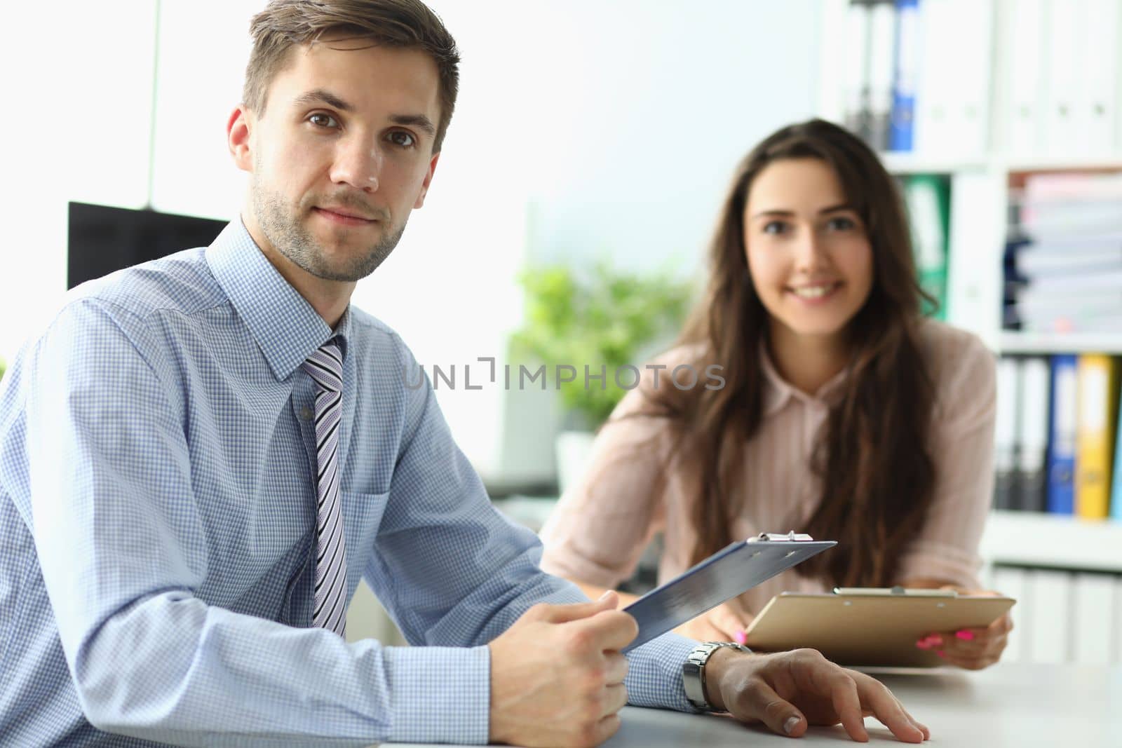 Businessman and businesswoman are sitting at table in office with documents by kuprevich