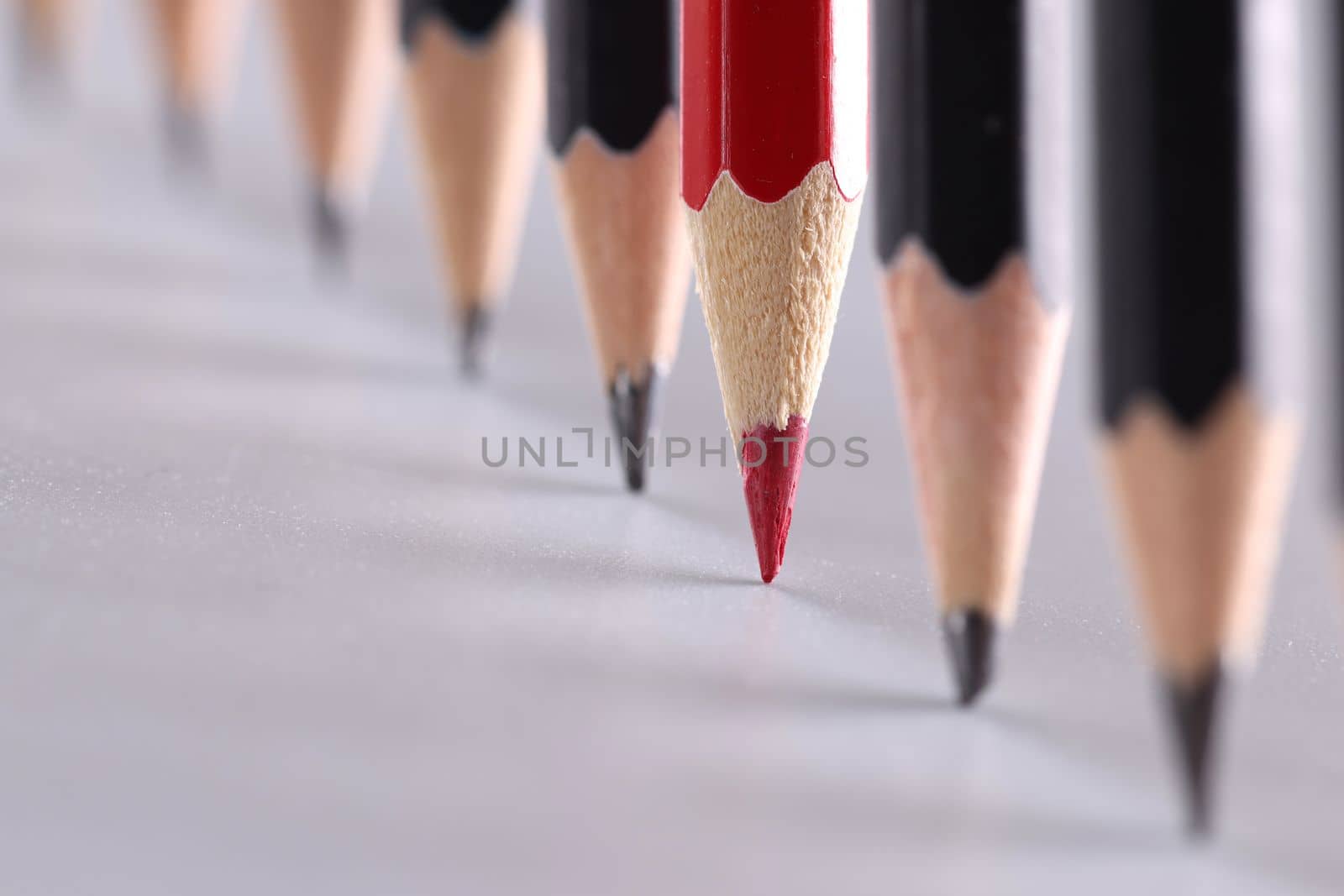 Red pencil stands out from crowd of many identical black pencils. Unique creative ideas for project
