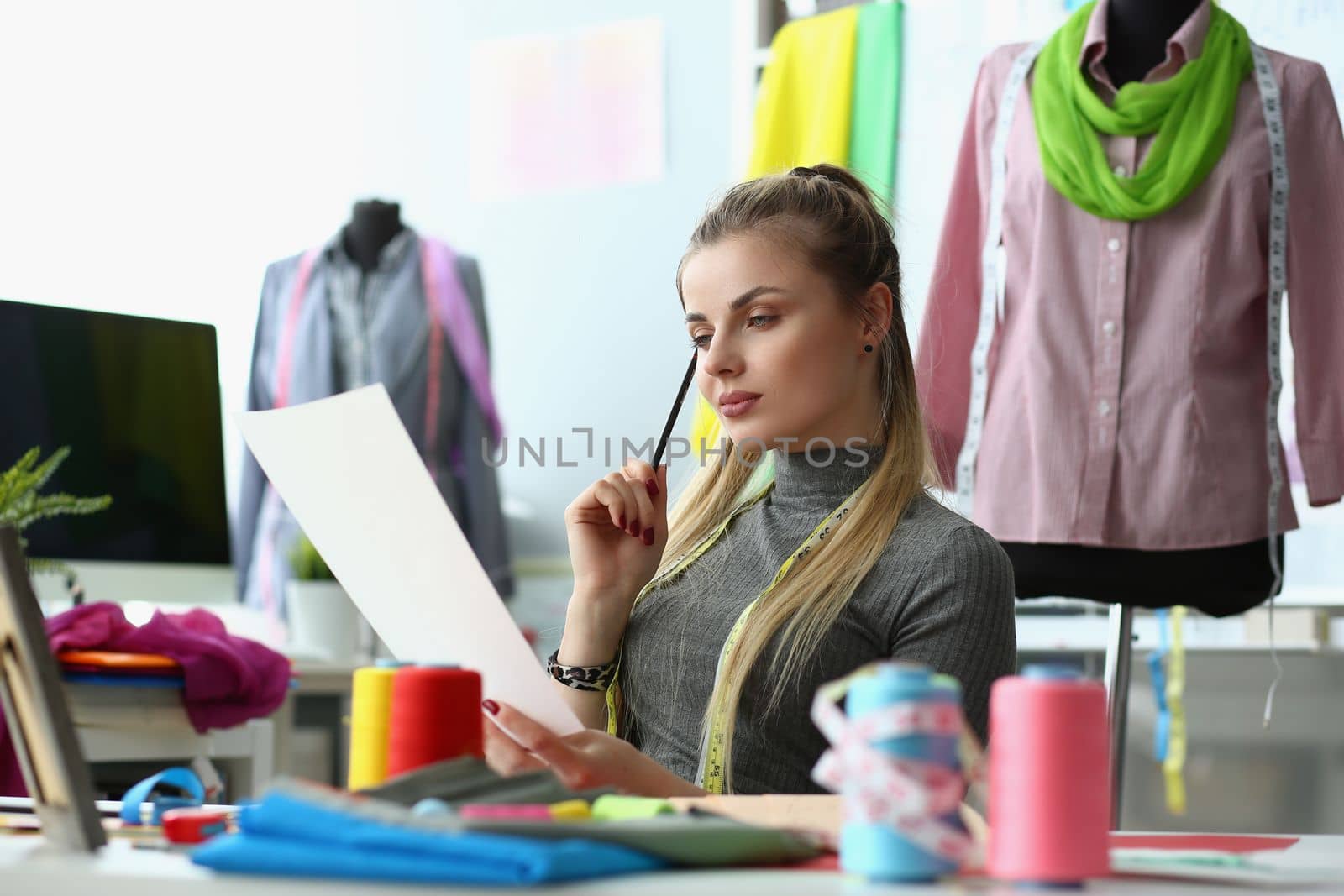 Woman designer are considering sketches of clothes at workplace in atelier by kuprevich