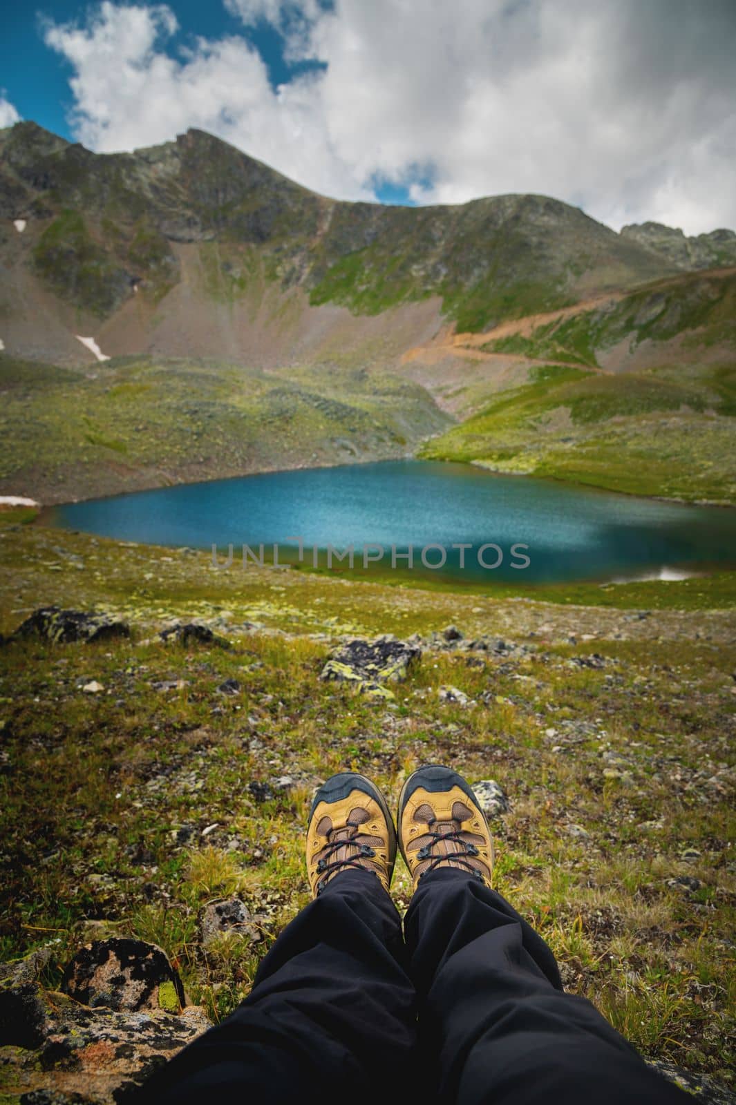 Feet of an alpine tourist in shoes against the backdrop of green mountains and an azure lake. hiking, solitude.