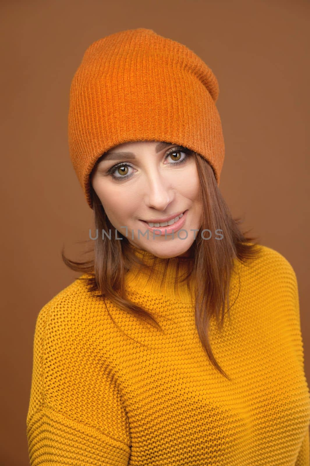 Portrait of a beautiful young woman in orange, in a sweater and a hat smiling, studio by yanik88
