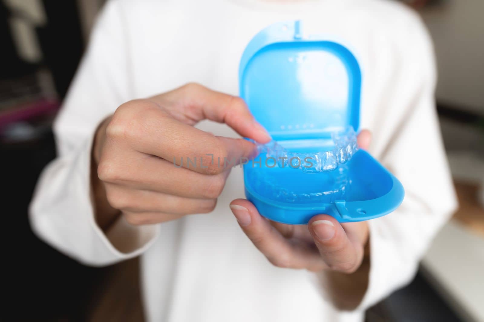 Close-up of a plastic transparent brace in the hand of a young woman, with a blue storage box. Selective focus by yanik88