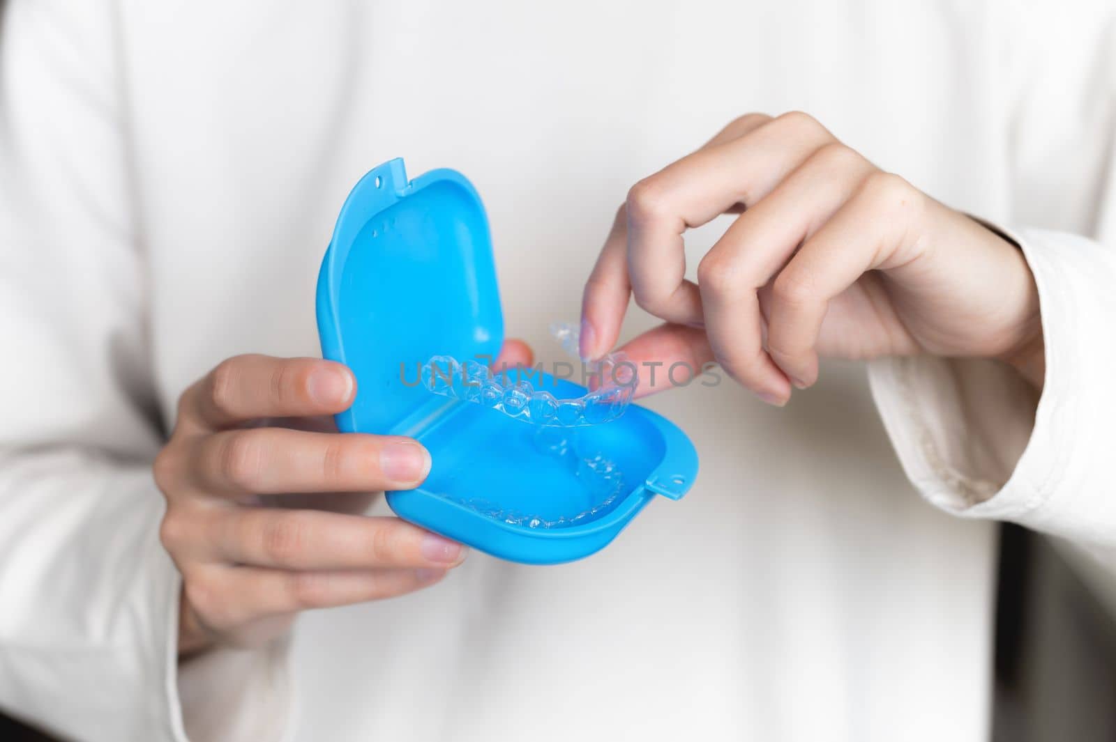 Close-up of a plastic transparent brace in the hand of a young woman, with a blue storage box. Selective focus by yanik88