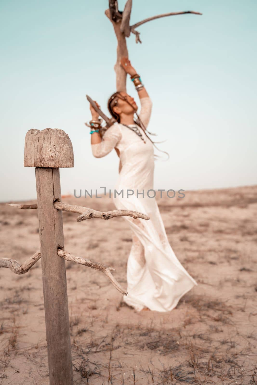 Model in boho style in a white long dress and silver jewelry on the beach. Her hair is braided, and there are many bracelets on her arms