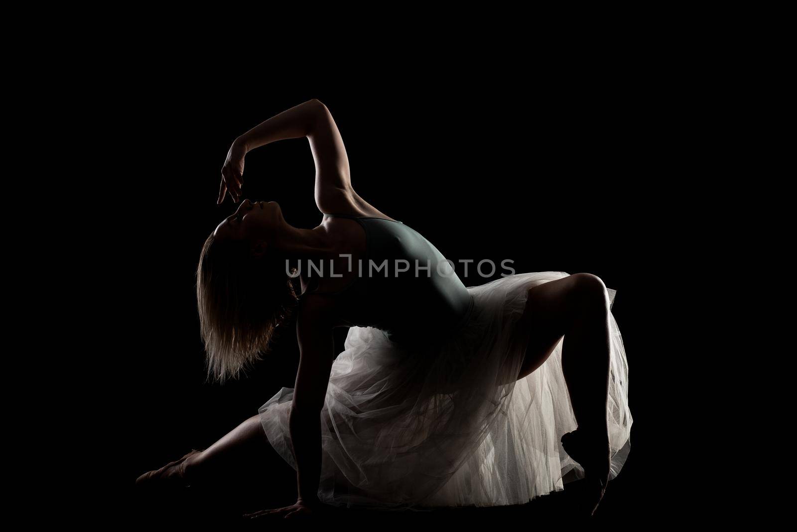 ballerina with a white dress and black top posing on black background. side lit silhouette