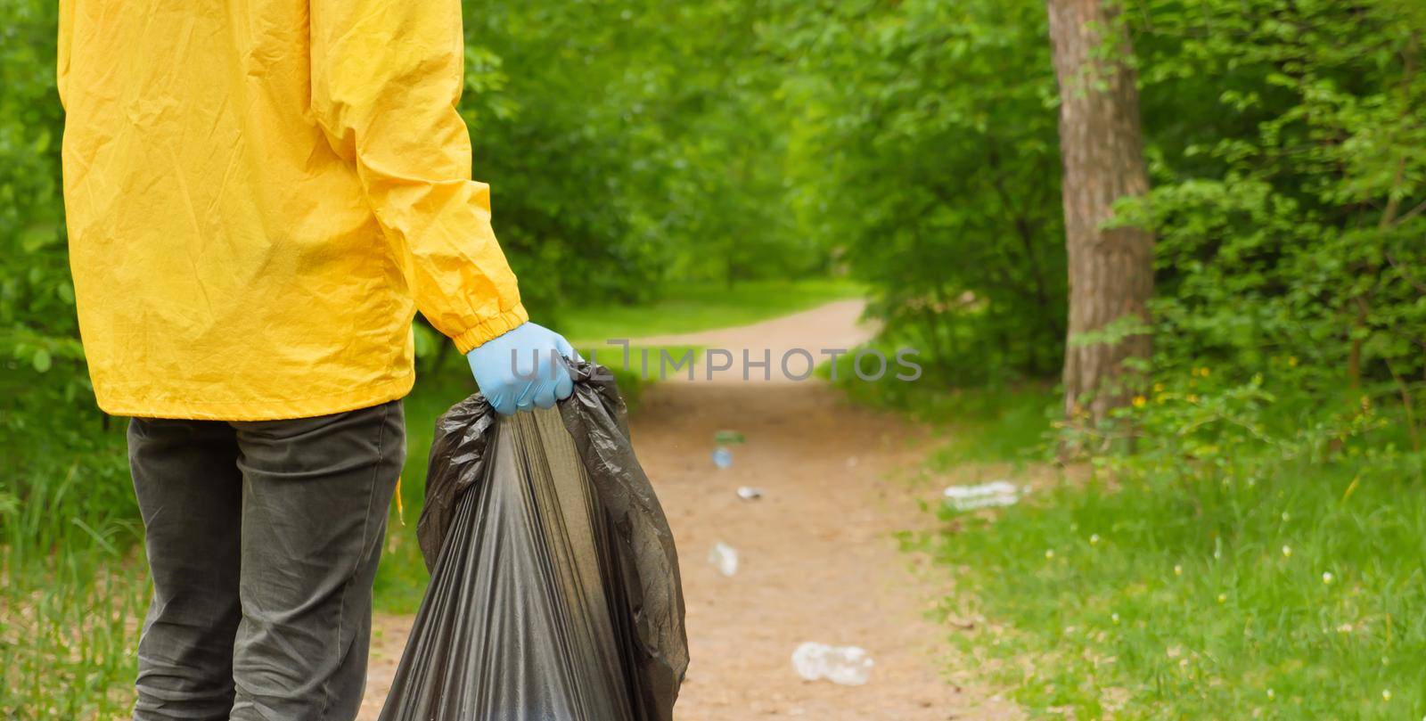 Volunteer cleaning up garbage a forest. People care earth pollution plastic garbage worker hand holding trash bag. Go green. Banner volunteer hands picks up a plastic trash grass in park. Eco friendly by synel