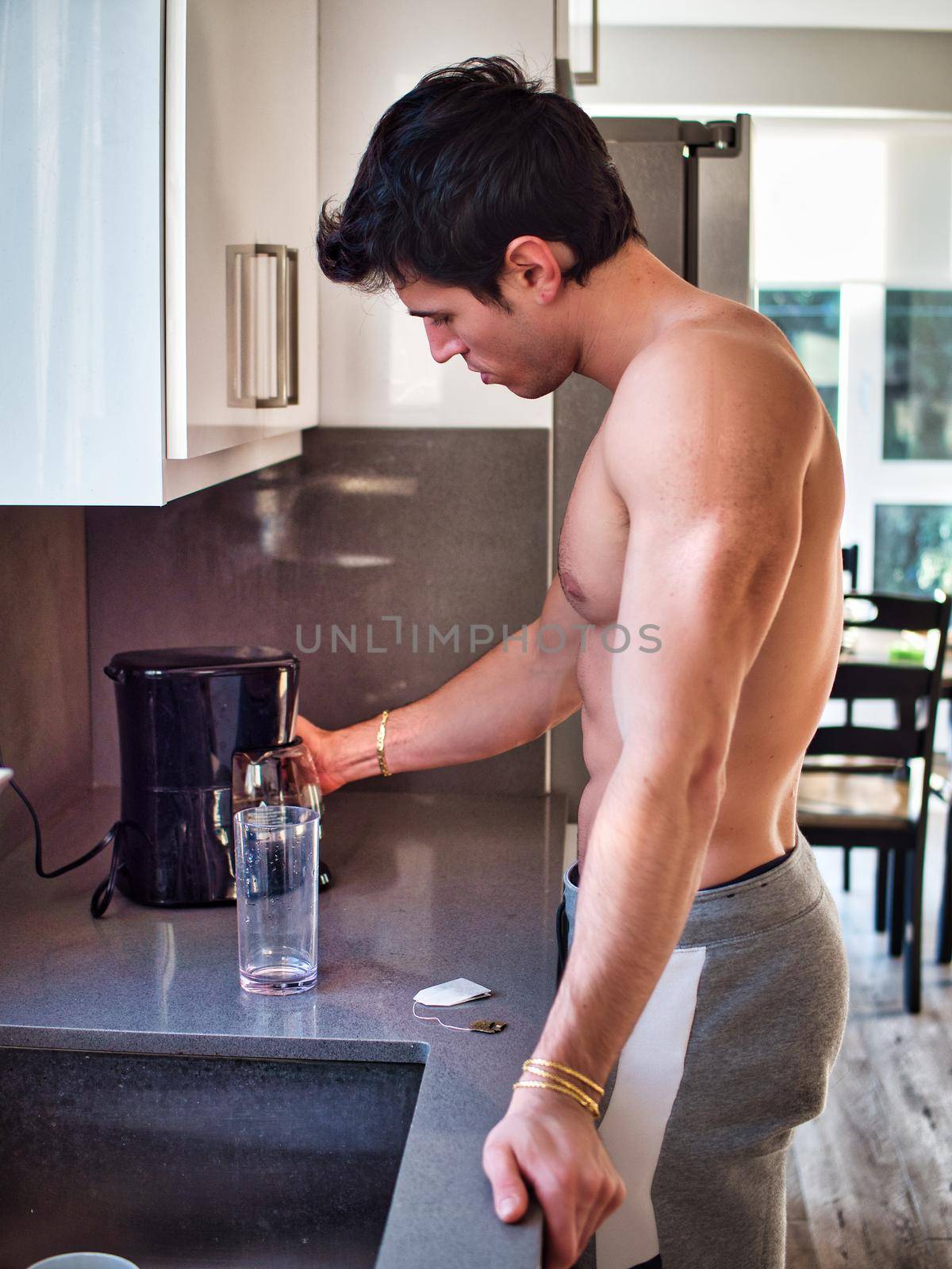 Side view of sexy muscular topless man in kitchen at home making coffee, wearing only sweatsuit pants