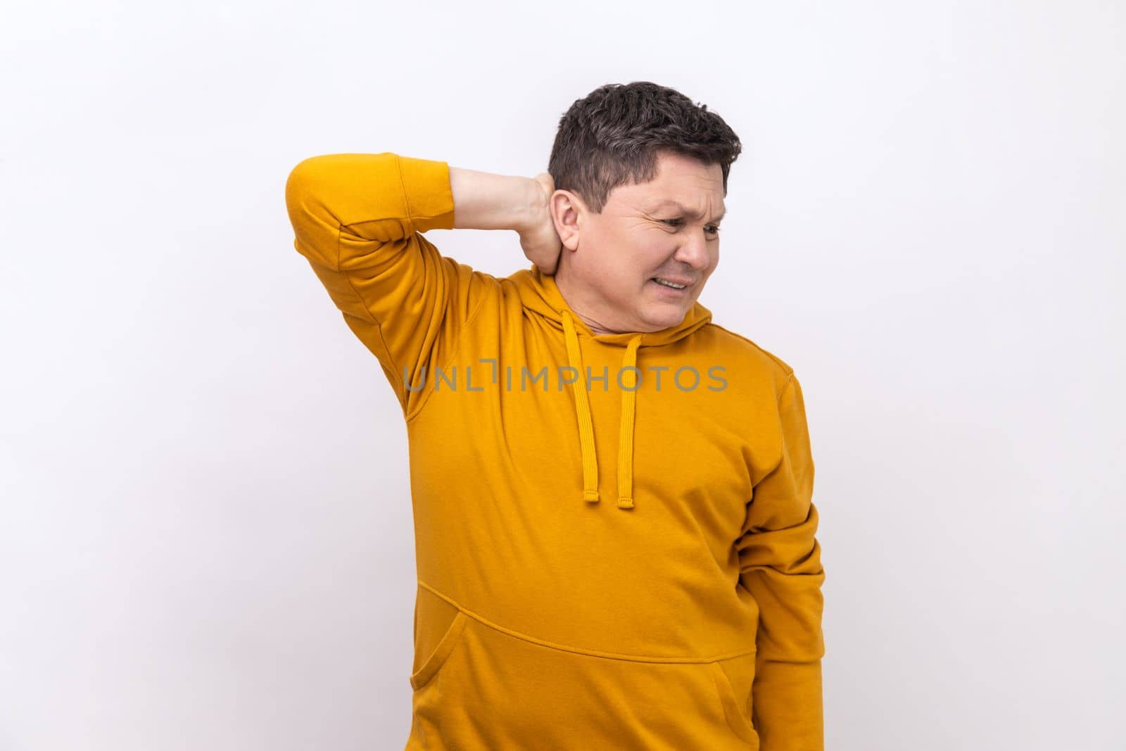 Worried anxious man touching neck, feeling acute pain moving and turning head, suffering spine problems, osteochondrosis, wearing urban style hoodie. Indoor studio shot isolated on white background.