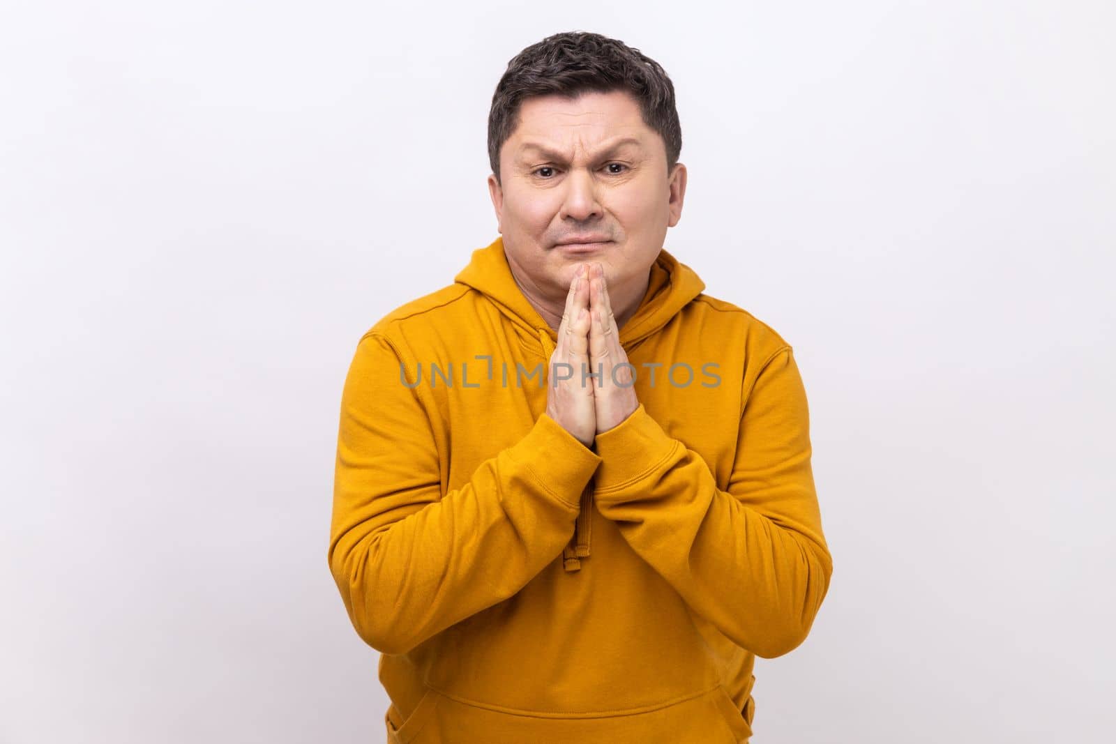 Please, I'm begging. Portrait of upset brunette man holding arms in prayer, asking help or forgiveness with imploring eyes, wearing urban style hoodie. Indoor studio shot isolated on white background.