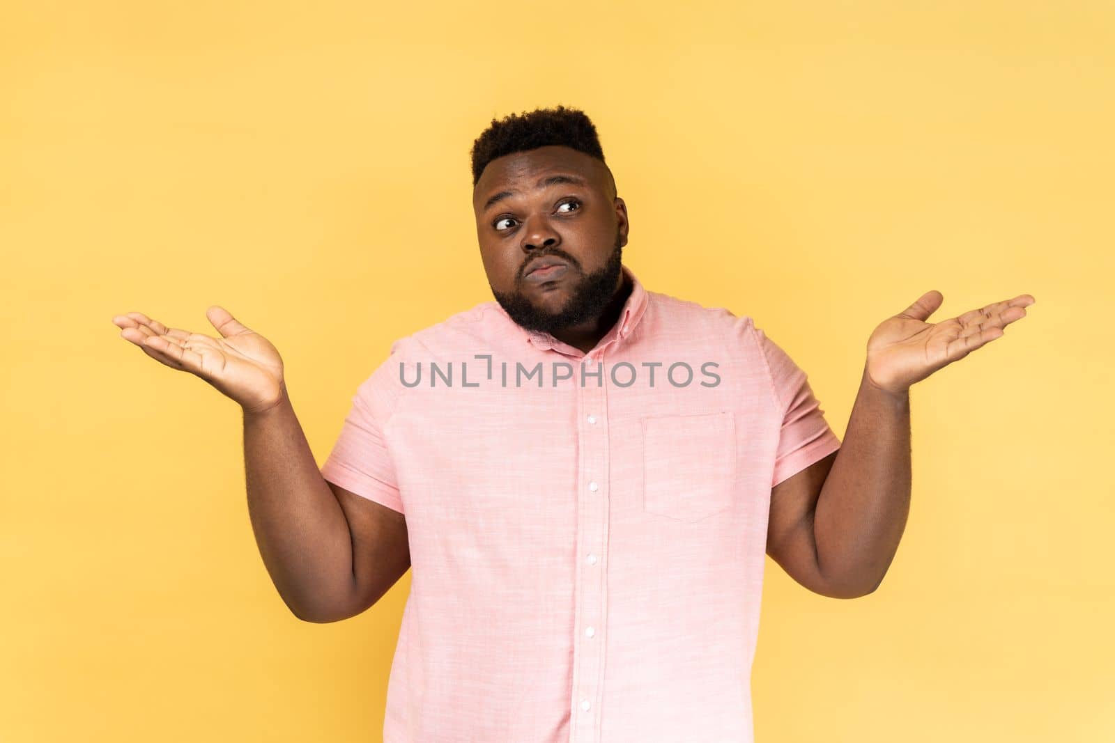 I dont know. Portrait of confused man wearing pink shirt shrugging shoulders as doesnt know answer, cant make decision, being uncertain, not sure. Indoor studio shot isolated on yellow background.