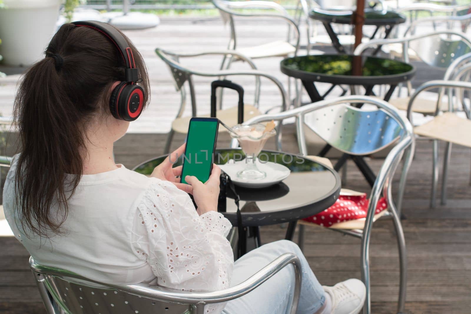 brunette girl listens to music in headphones with a green screen phone, at a table in a cafe, High quality photo