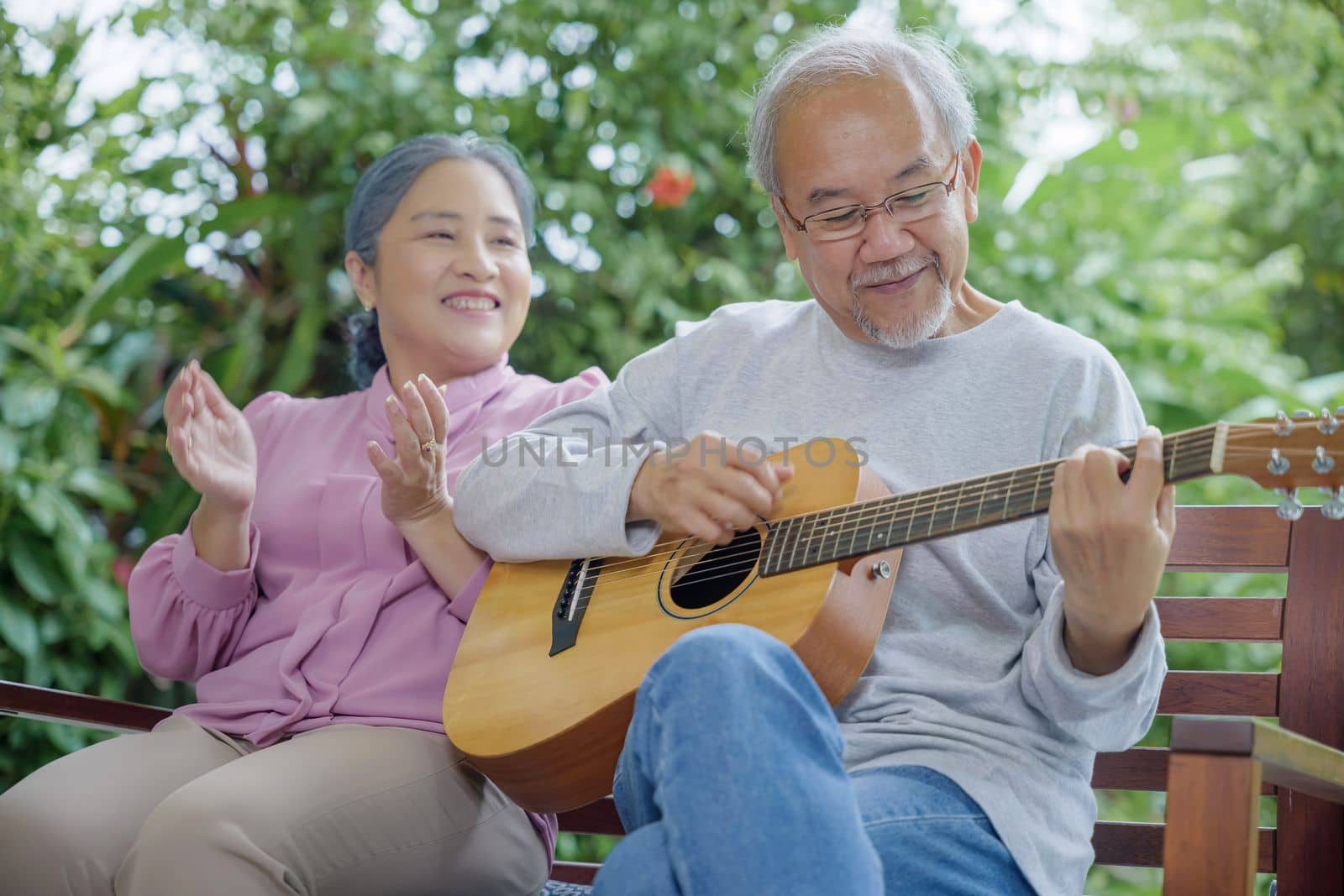 Happy two Asian senior couple elderly man playing the guitar while his wife is singing together at home outdoors, Enjoying lifestyle during retirement life having fun, Activity family health care