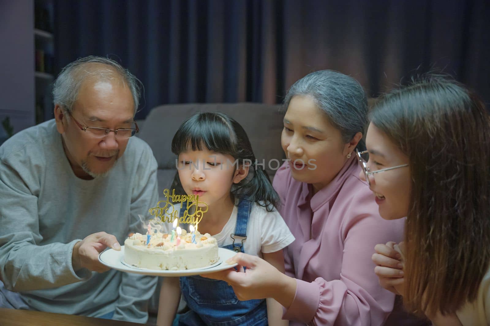 Birthday surprise. Happy Asian family grandparents and mother celebrating enjoy birthday party with cake of granddaughter at home in night time