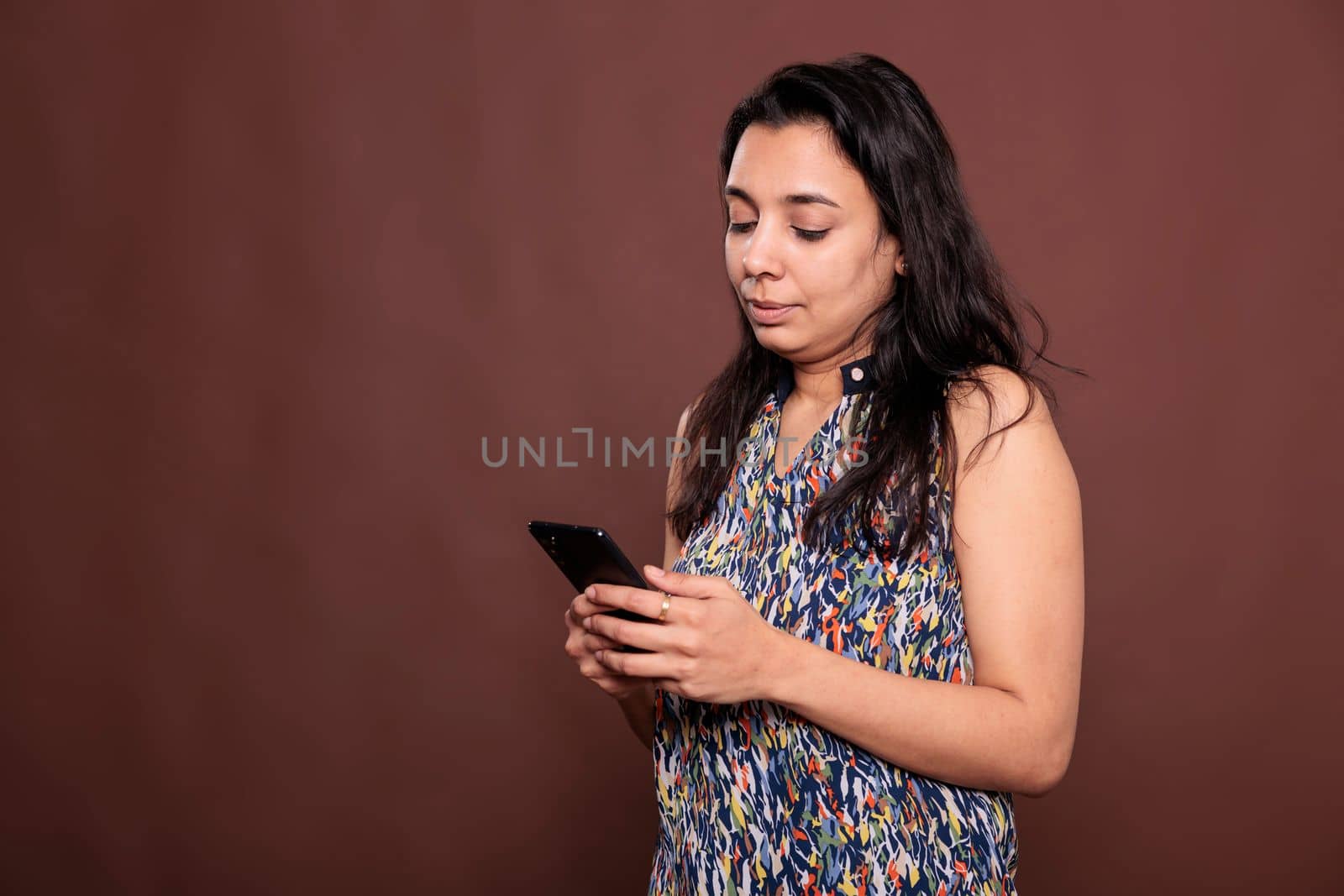 Indian woman chatting in social networks, using smartphone, sending text messages. Serious lady holding mobile phone, talking online, texting on telephone, studio medium shot