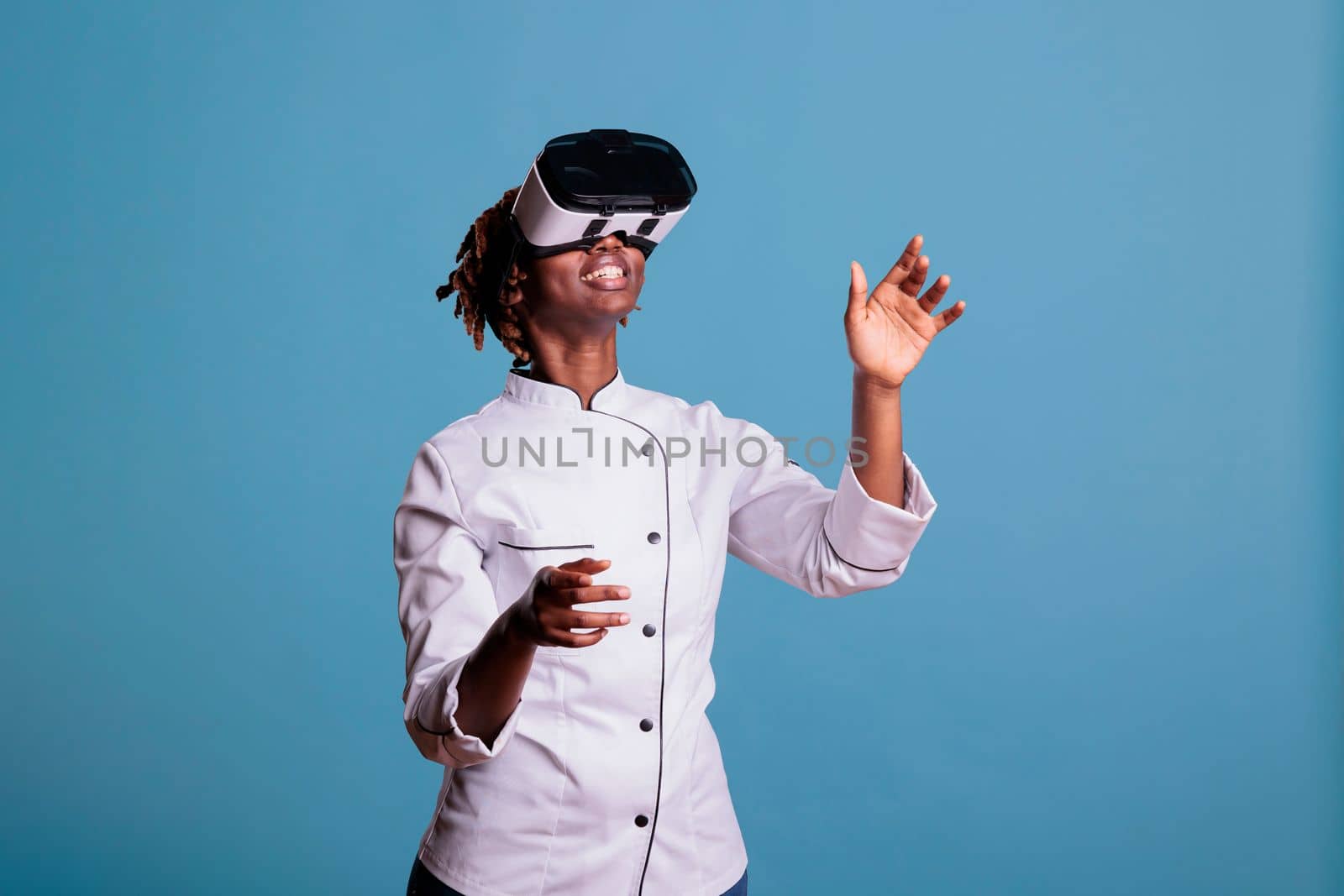 Professional female chef in uniform playing virtual reality games with VR goggles, exploring simulations. African american cook moving arms while touching objects in cyberspace.