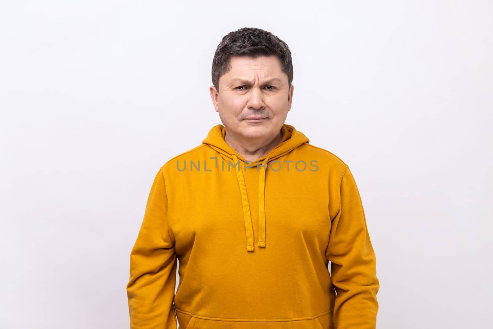 Portrait of sad upset dark haired man standing and looking at camera with dissatisfied sadness face, expressing sorrow, wearing urban style hoodie. Indoor studio shot isolated on white background.