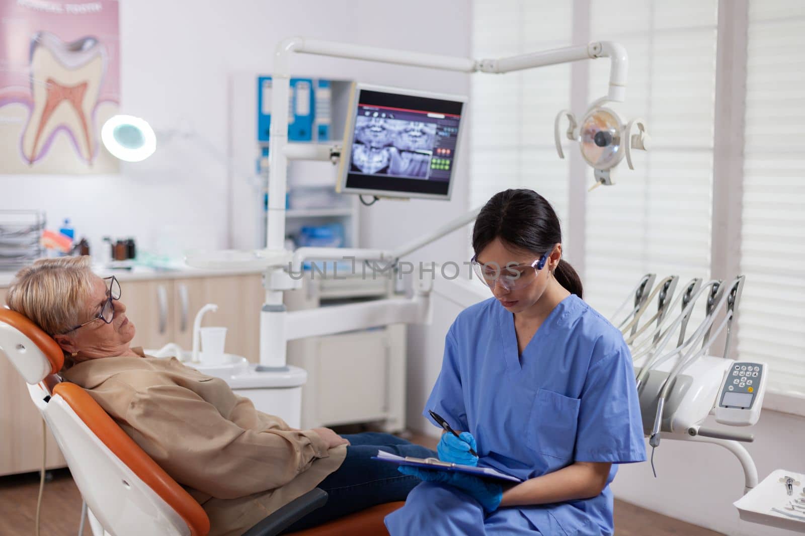 Dental assistant completing questioner during oral checkup of elderly patient. Senior woman talking with medical nurse in stomatology office about teeth problem.