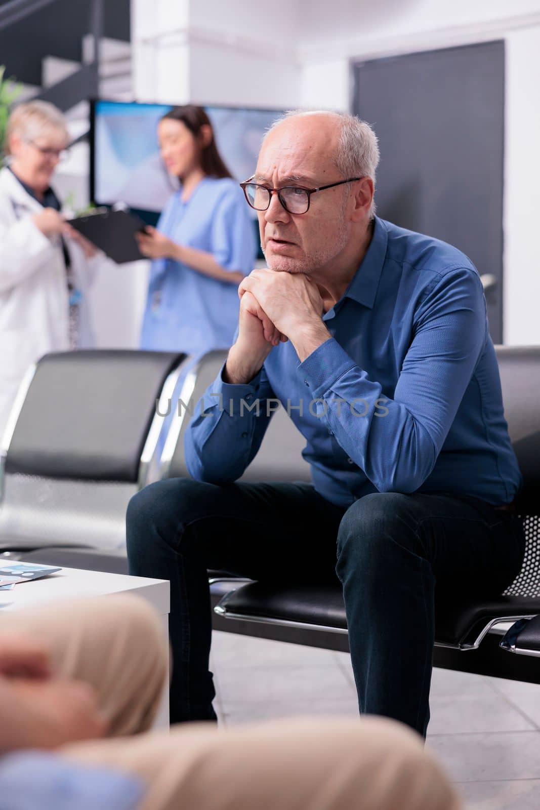 Exhausted elderly patient sitting on chair in hospital reception while waiting for physician doctor by DCStudio