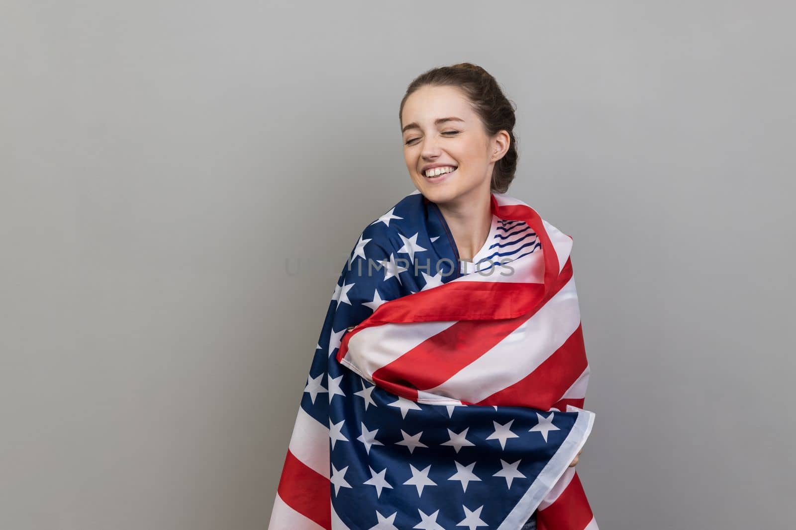 Woman wrapped in USA flag, expressing happiness, posing with closed eyes and toothy smile. by Khosro1