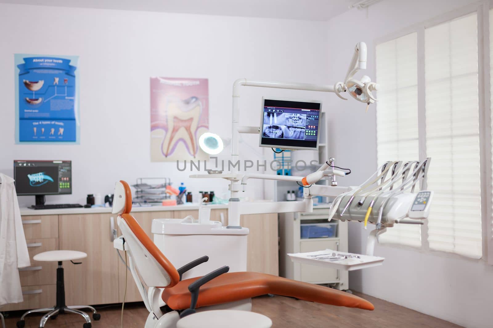 Interior of empty operating room in dental clinic. Stomatology cabinet with nobody in it and orange equipment for oral treatment.