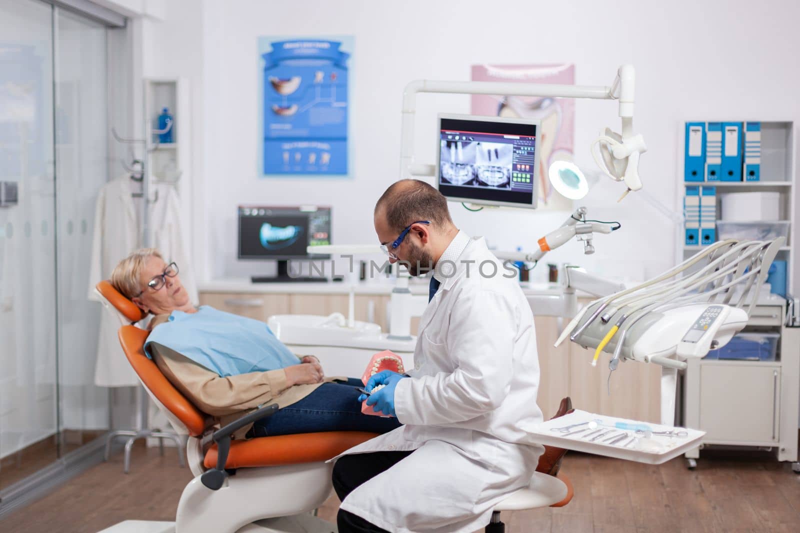 Senior woman discussing with dentist in dental cabinet about teeth issue sitting on chair. Medical teeth care taker discussing with senior woman about mouth hygiene.