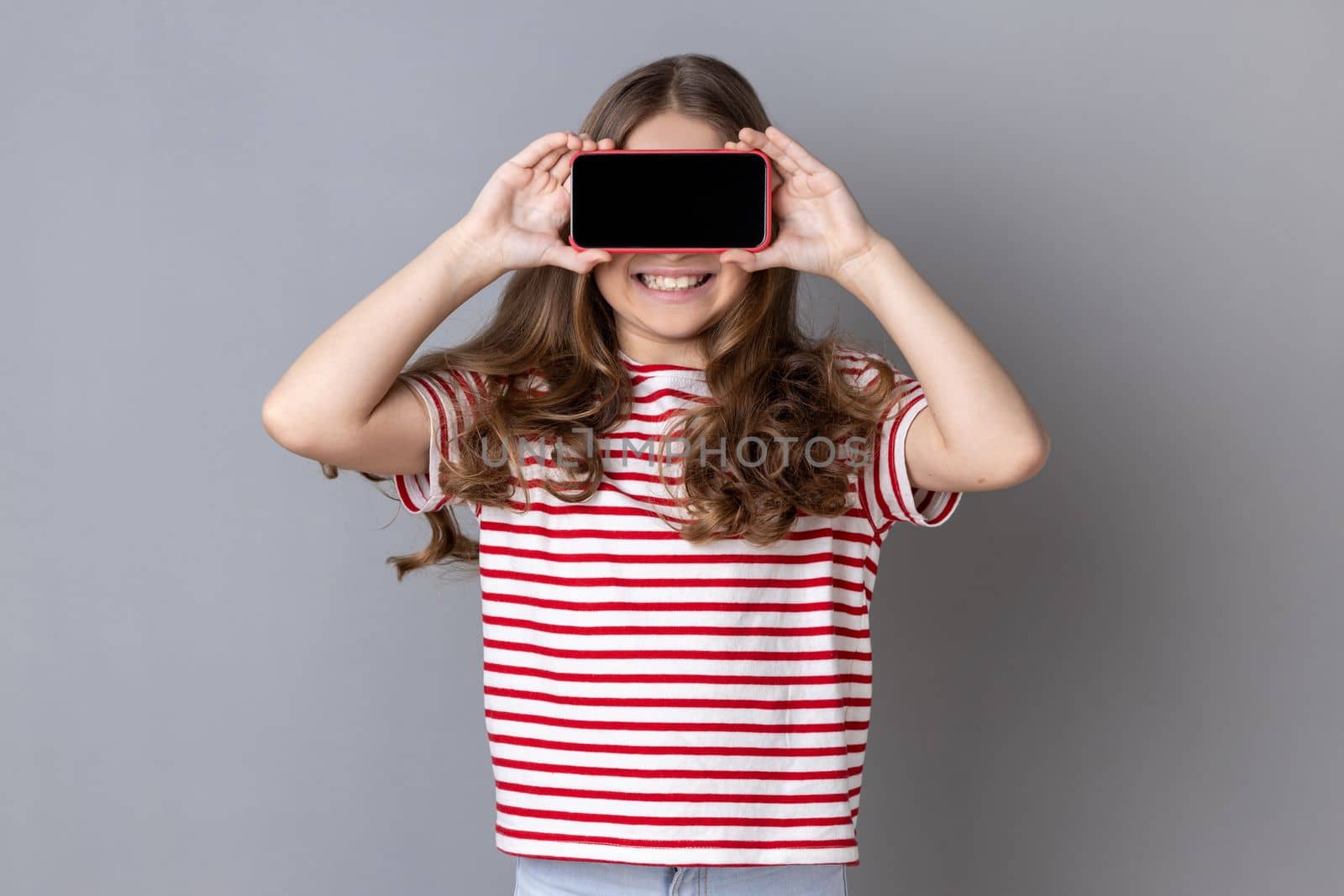 Little girl covering eyes with cellphone and smiling, unknown child hiding face with mobile phone. by Khosro1