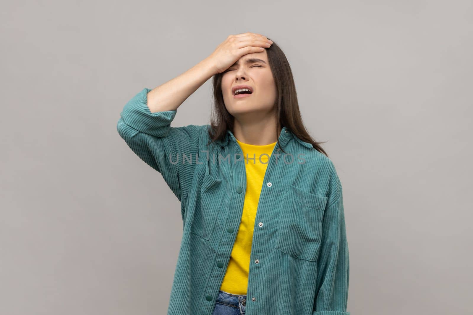 Unlucky woman with facepalm gesture, feeling regret and sorrow, blaming herself for mistake, frustrated by defeat, wearing casual style jacket. Indoor studio shot isolated on gray background.