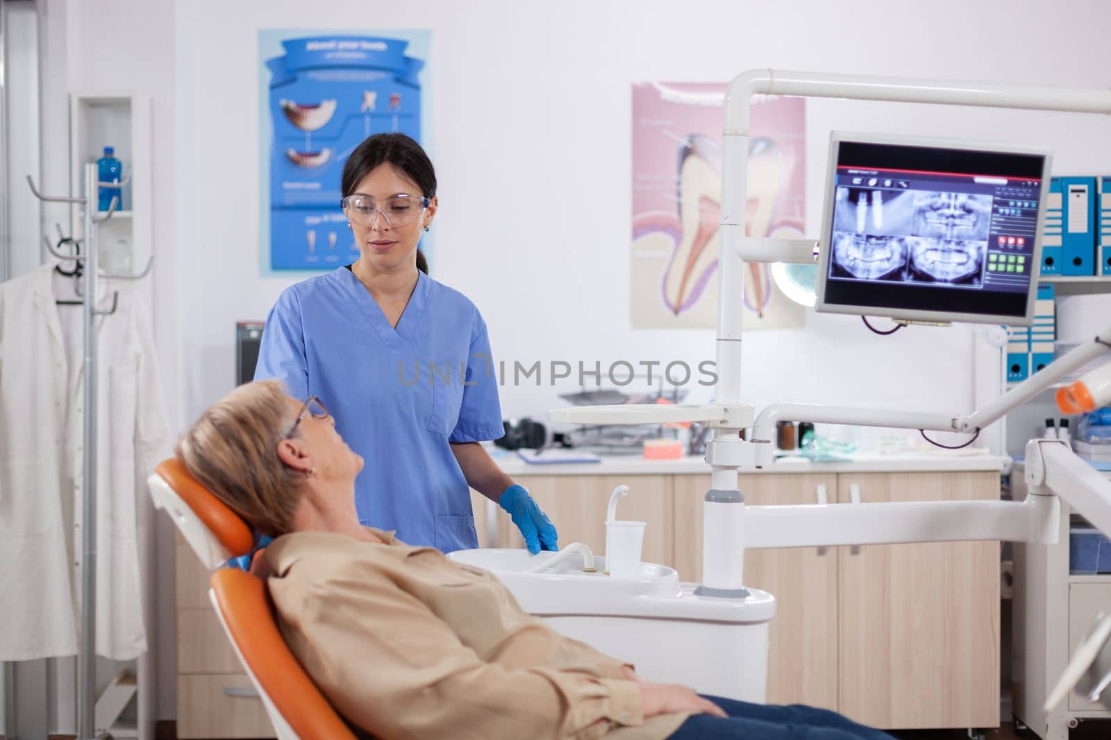 Assistant in dental clinic questioning elderly patient by DCStudio