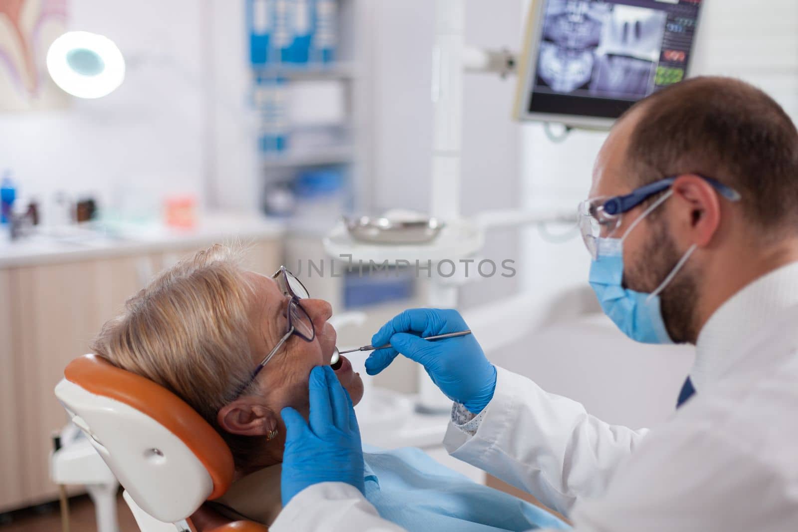 Stomatolog with senior client examining a patient teeth Elderly woman during medical examination with dentist in dental office with orange equipment.