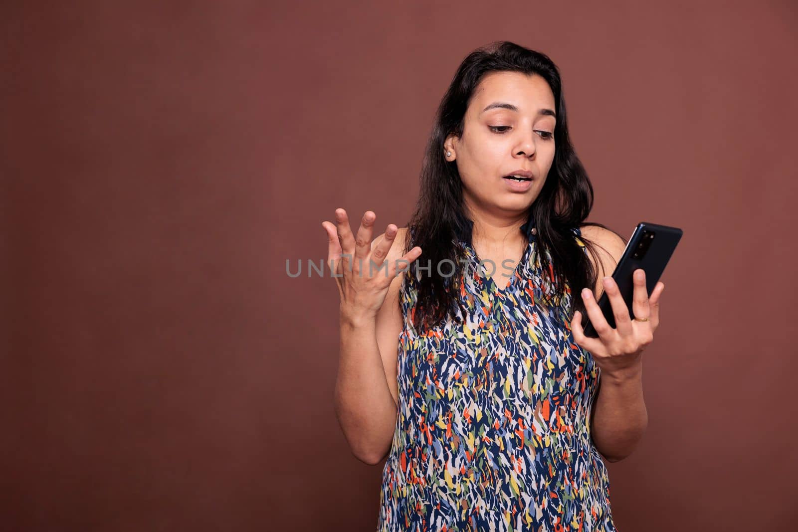 Irritated indian woman using smartphone app, reading news on internet. Confused person holding mobile phone, messaging in social networks, texting, looking at telephone screen