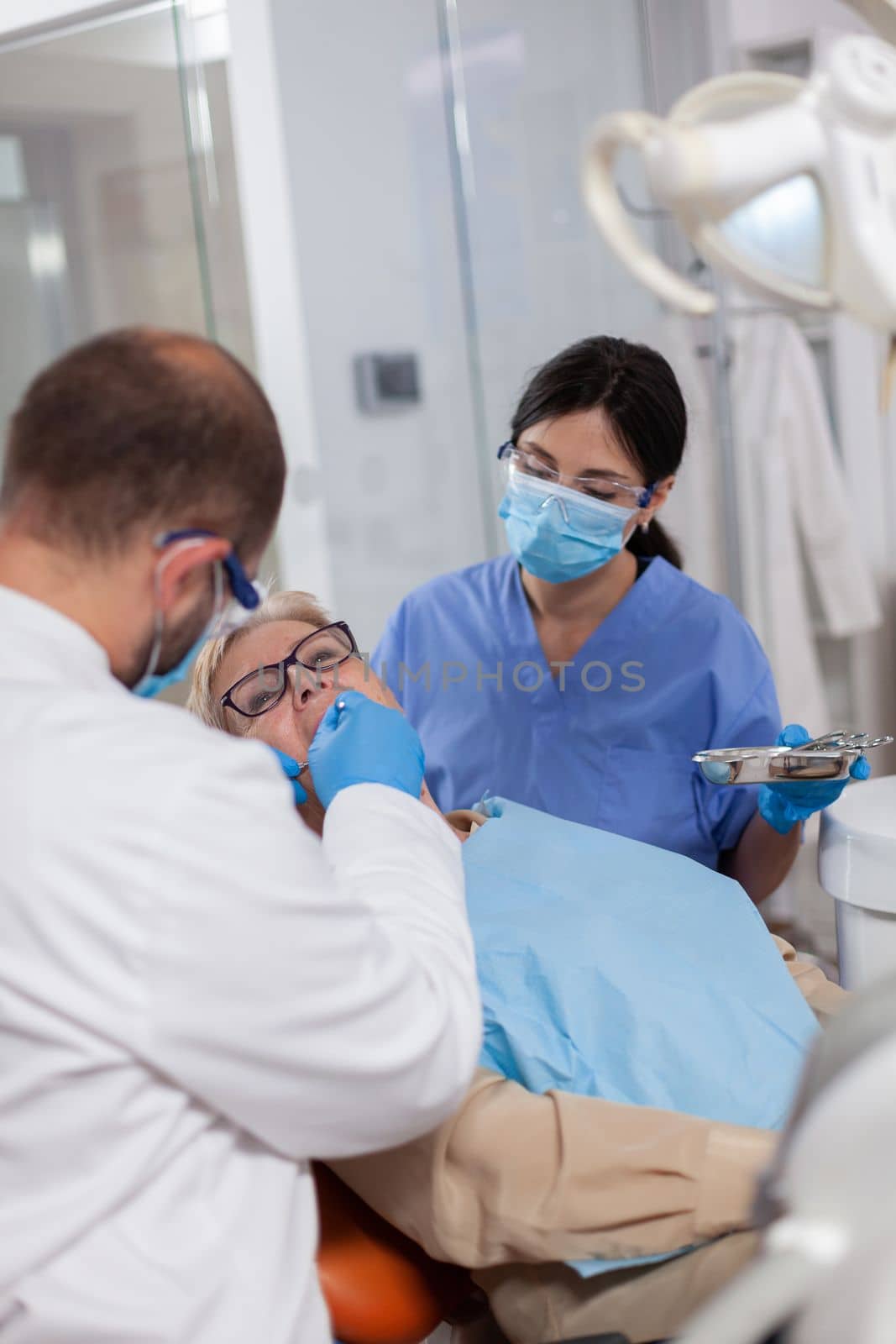 Dentist with assistant install implant in patient mouthin modern clinic. Elderly woman during medical examination with stomatolog in dental office with orange equipment.