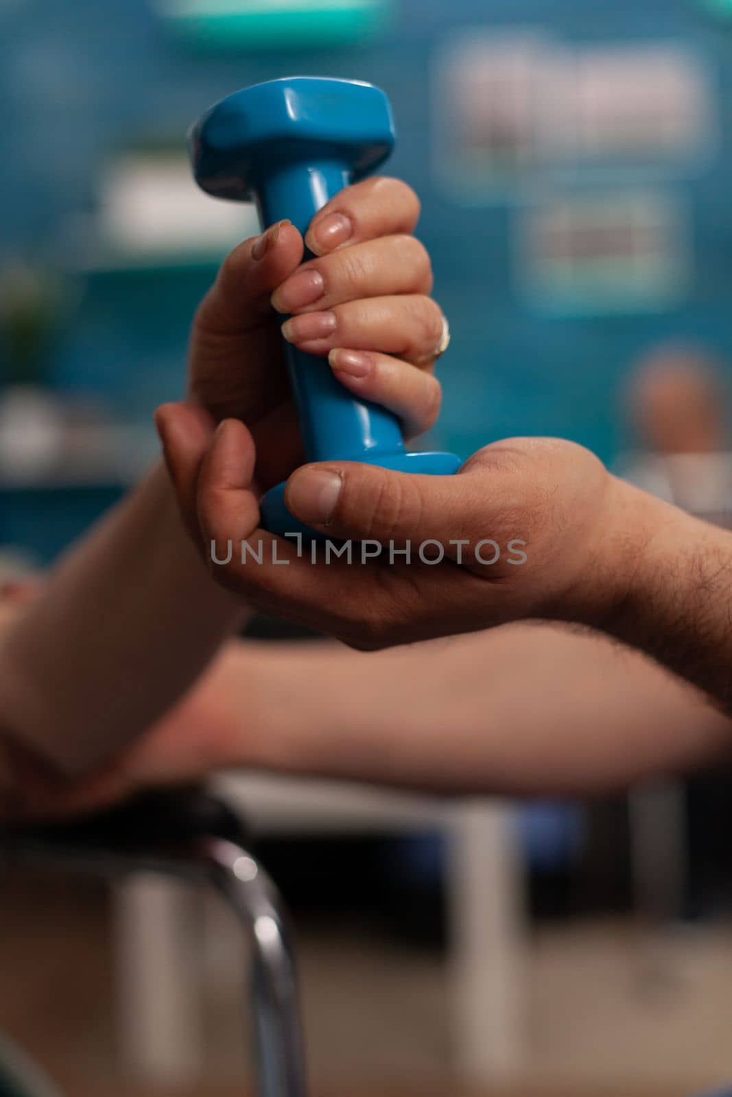 Female hand holding weights while male therapist helps her with exercises in nursing home. Specialized center for care and physical therapy of elderly people with disabilities, close up.