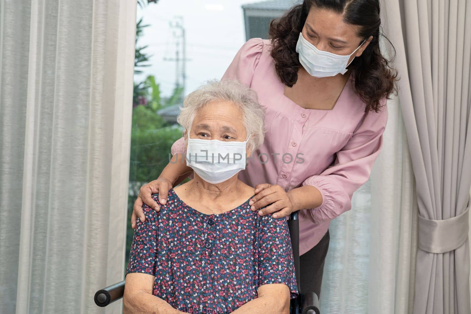 Caregiver help Asian senior or elderly old lady woman sitting on wheelchair and wearing a face mask for protect safety infection Covid19 Coronavirus. by pamai