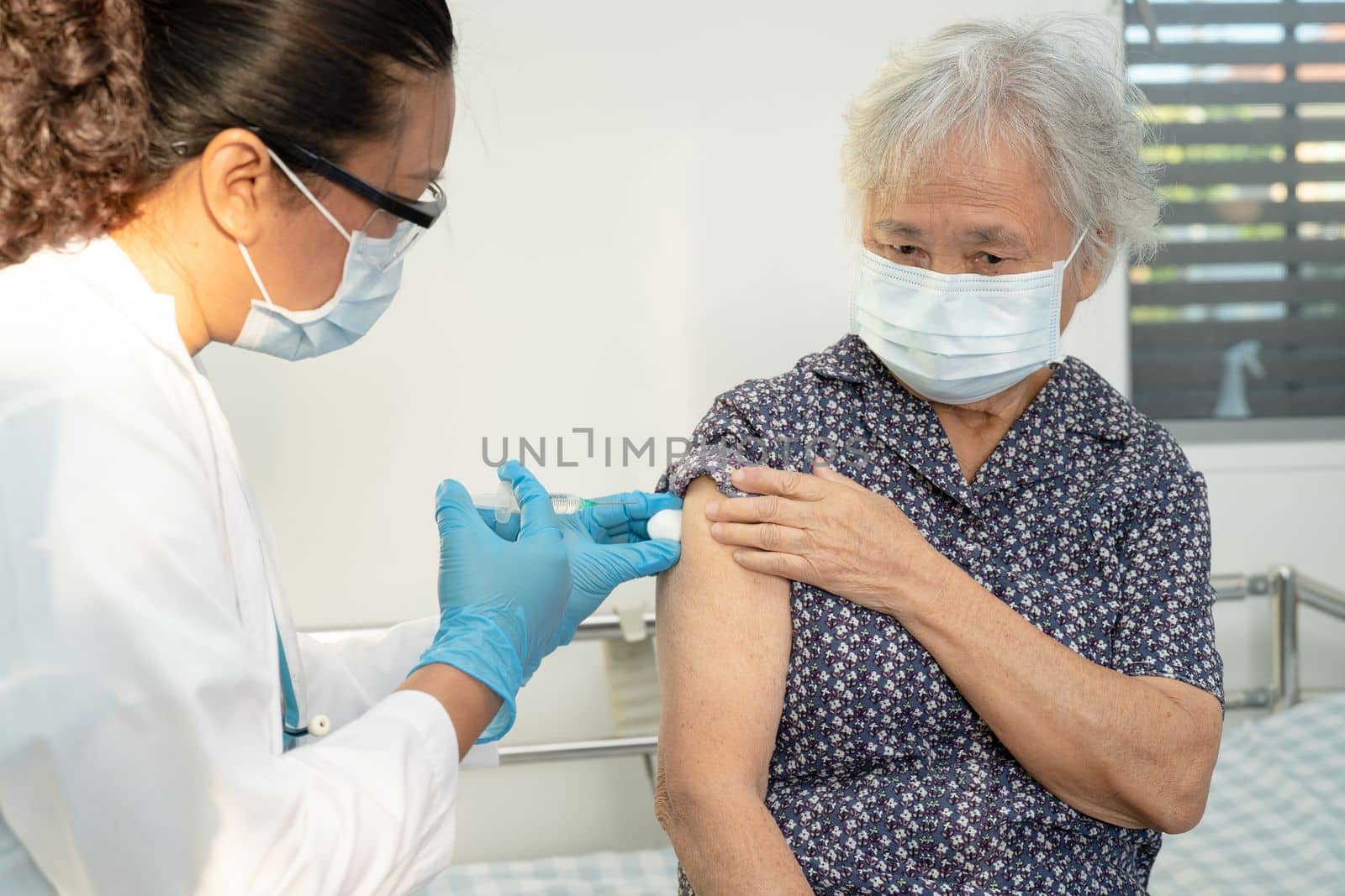 Elderly Asian senior woman wearing face mask getting covid19 or coronavirus vaccine by doctor make injection. by pamai