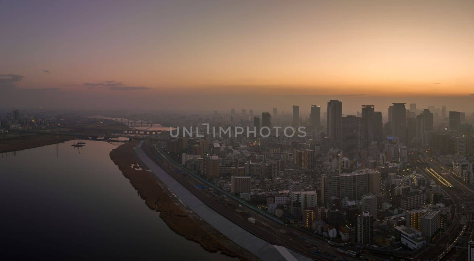 Hazy sunrise over high rise buildings in sprawling city next to river by Osaze