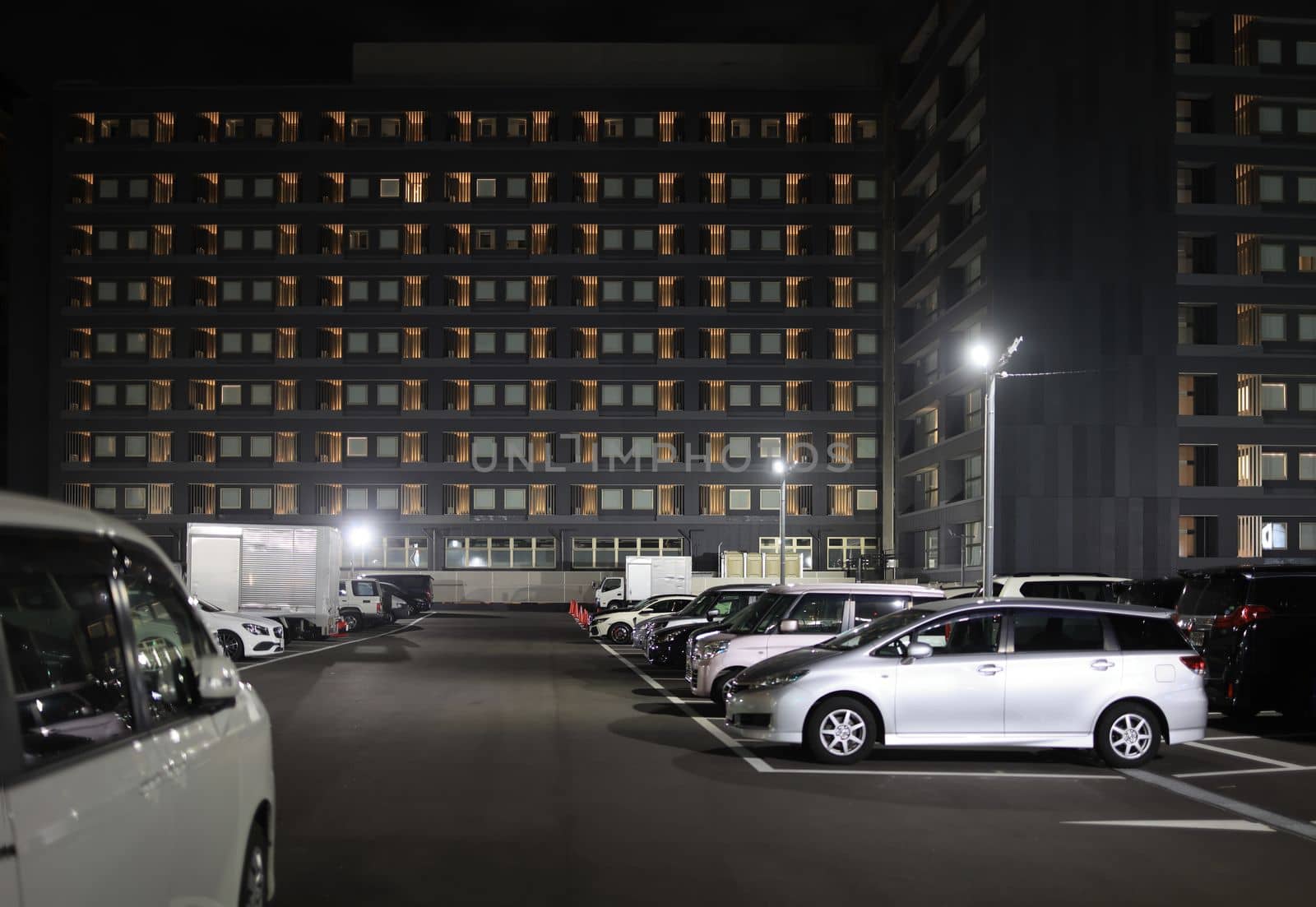 Full parking lot by multi-story building at night. High quality photo