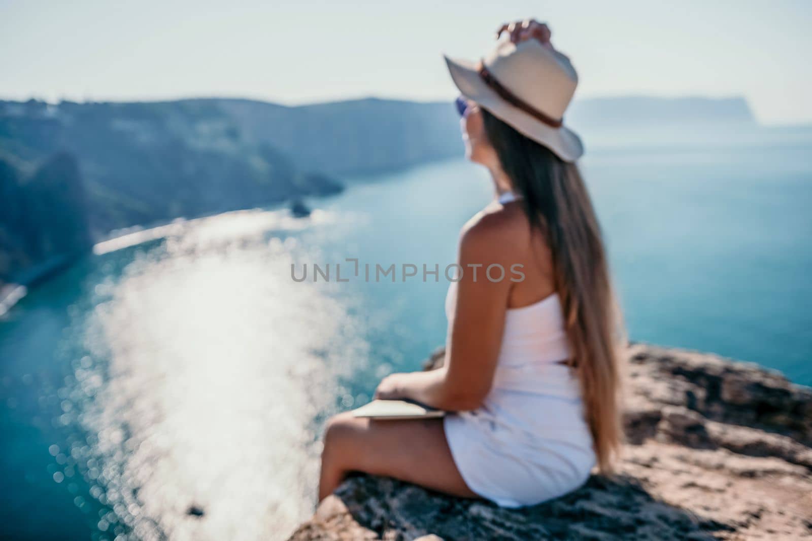 Successful business woman in yellow hat working on laptop by the sea. Pretty lady typing on computer at summer day outdoors. Freelance, travel and holidays concept.