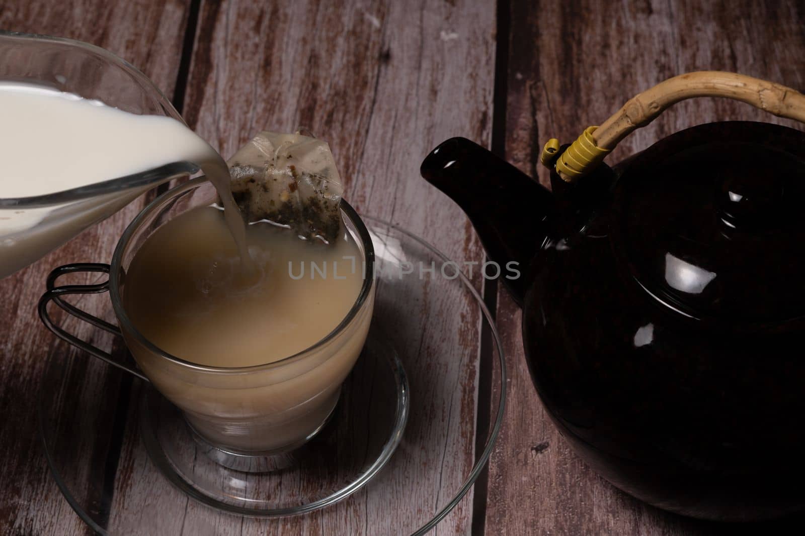 tea cup and teapot pouring hot tea on a wooden table and black background with copy-space