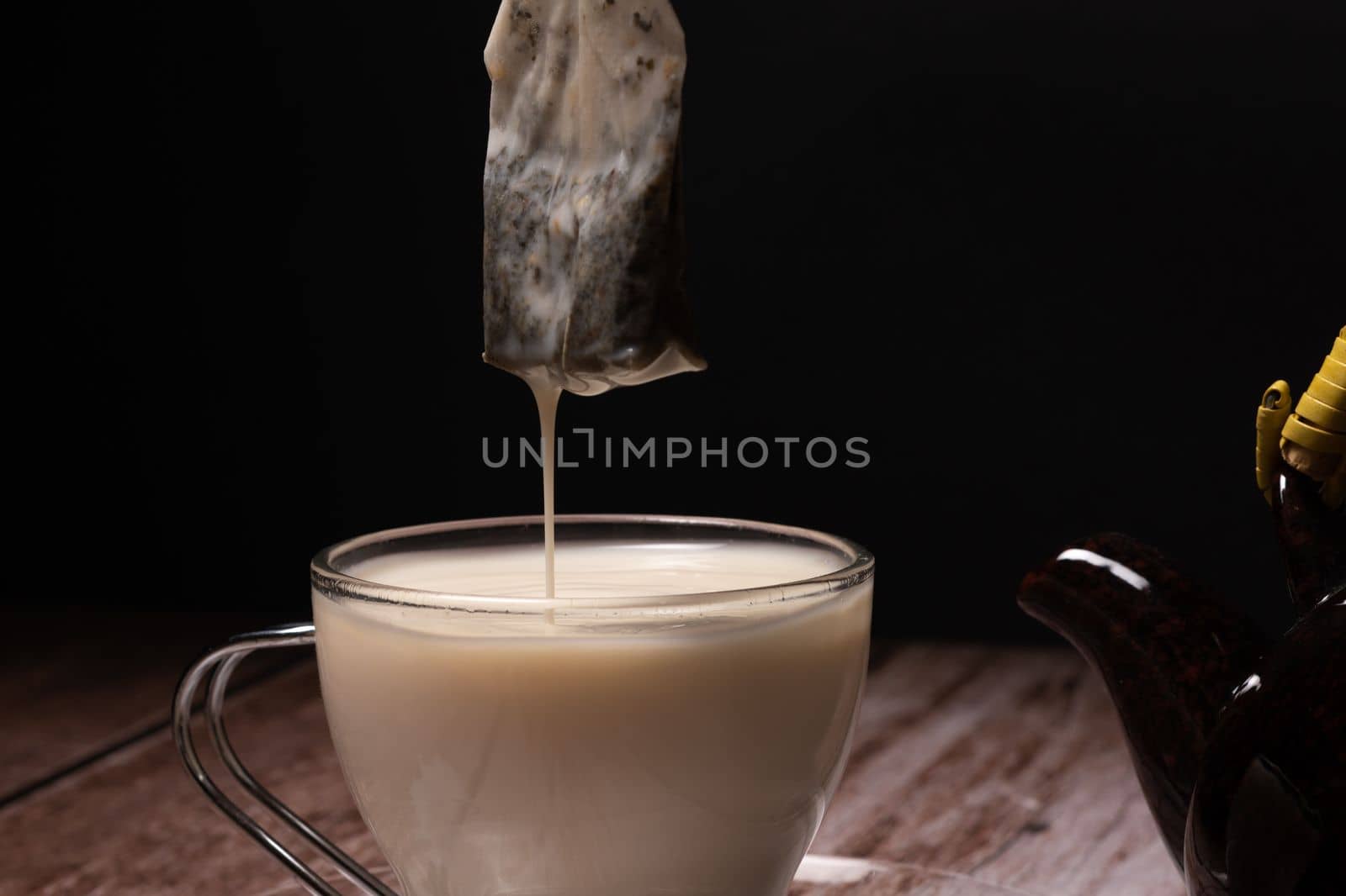 tea cup and teapot pouring a cloud of hot milk on a wooden table by joseantona