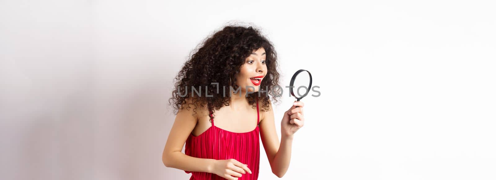 Beautiful woman in red dress and makeup looking at something with magnifying glass, checking out interesting promo, standing over white background by Benzoix
