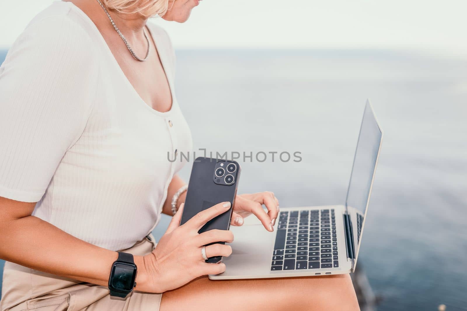 Digital nomad, Business woman working on laptop by the sea. Pretty lady typing on computer by the sea at sunset, makes a business transaction online from a distance. Freelance, remote work on vacation by panophotograph