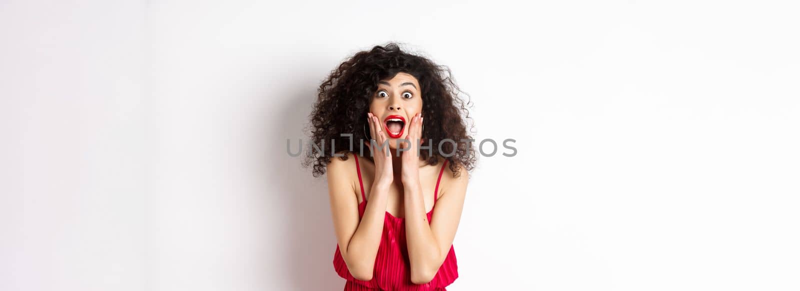 Image of elegant woman scream surprised, staring at camera, see promo offer and shouting of joy, standing in dress over white background.